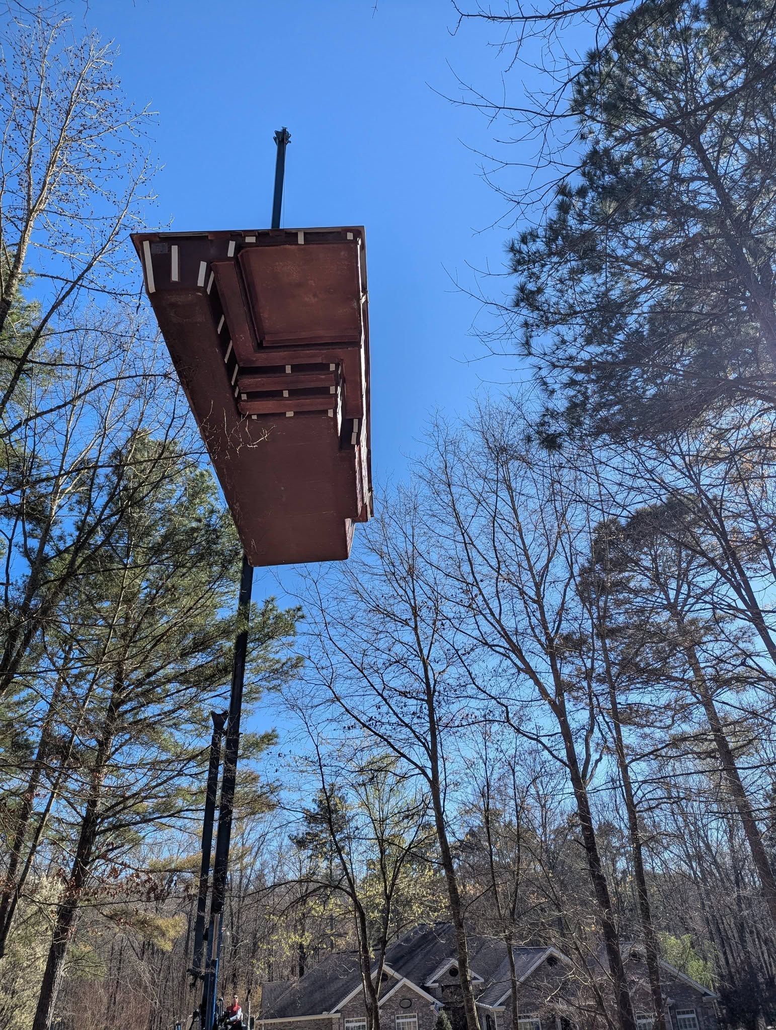 Rust-colored roof platform suspended among tall trees under a clear blue sky