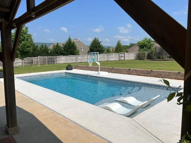 Backyard swimming pool with diving board, fence, and sunny blue sky