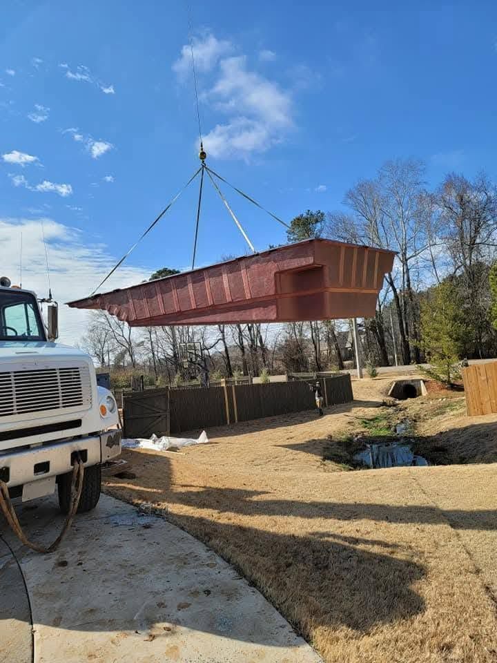 Red prefab cabin being lifted by crane over a gravel lot beside a truck under a blue sky