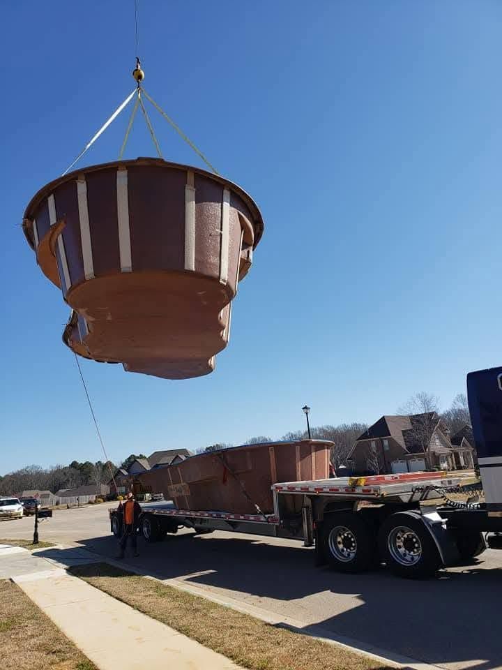Large rust-colored metal tank being lifted by crane onto a flatbed trailer on a sunny street