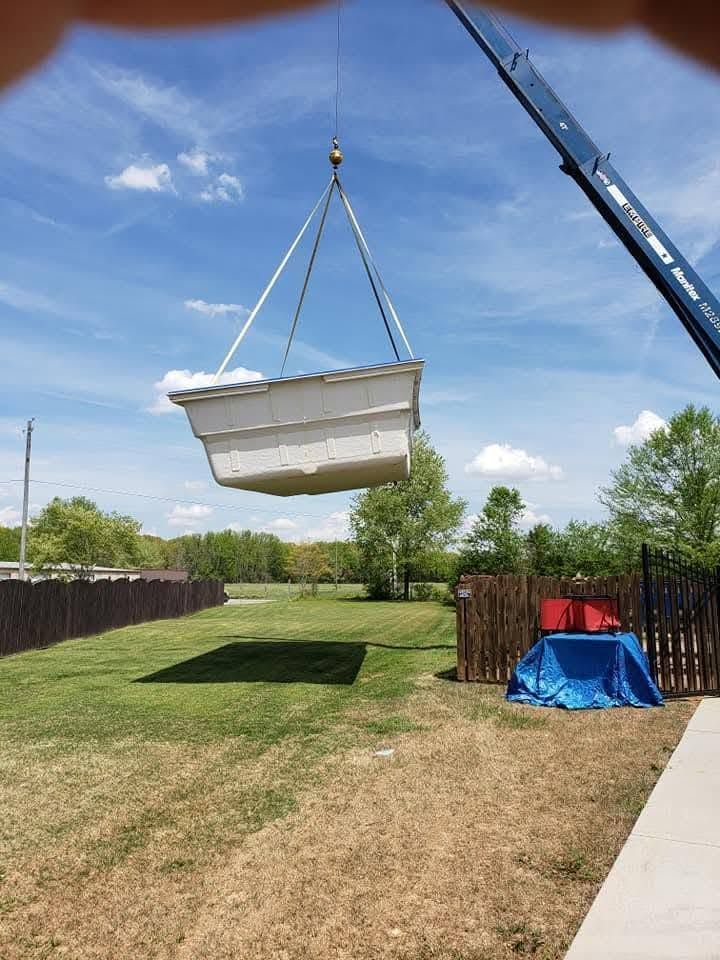Large white container suspended by crane over a grassy backyard under a blue sky