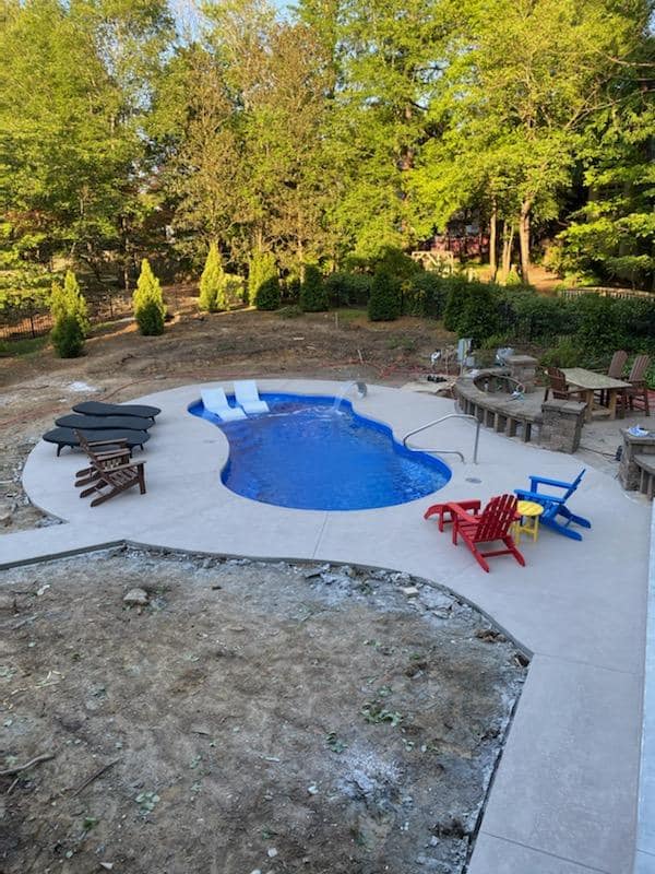 Backyard with a small blue pool, concrete patio, and colorful chairs surrounded by trees