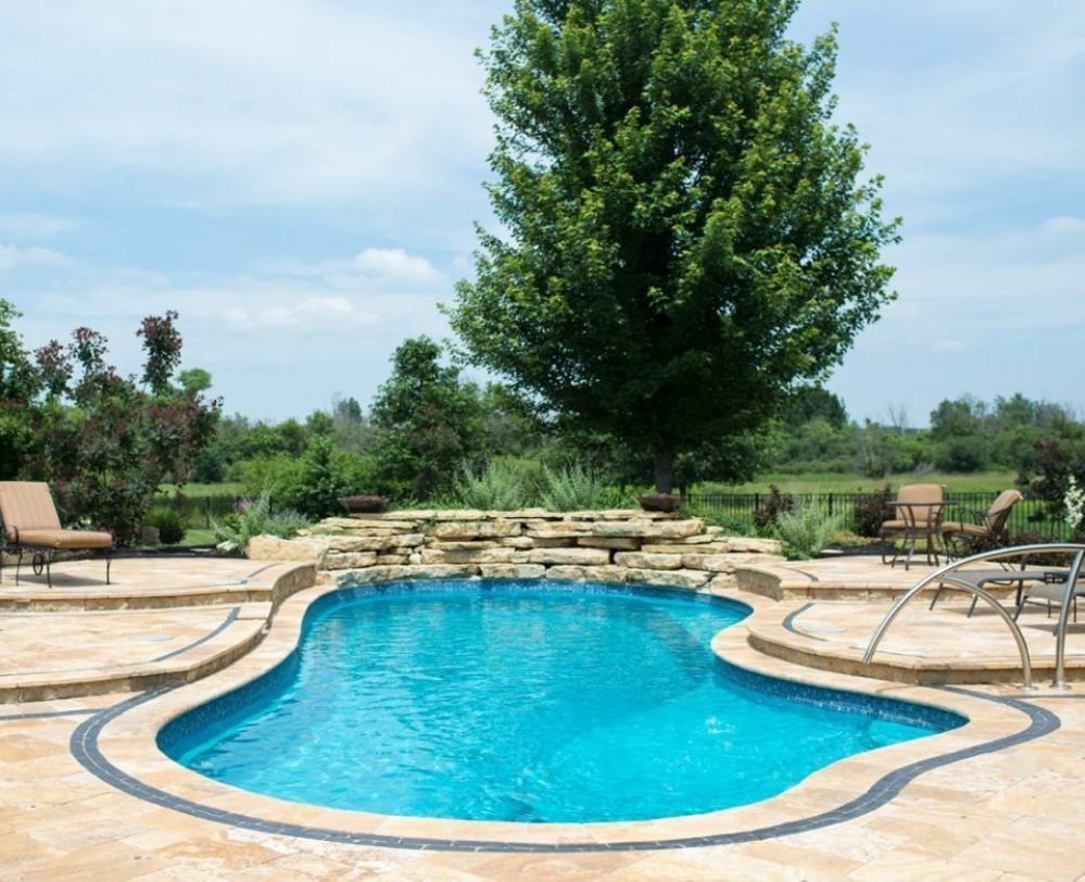 Backyard swimming pool with stone deck, lounge chairs, and a large tree beyond the water