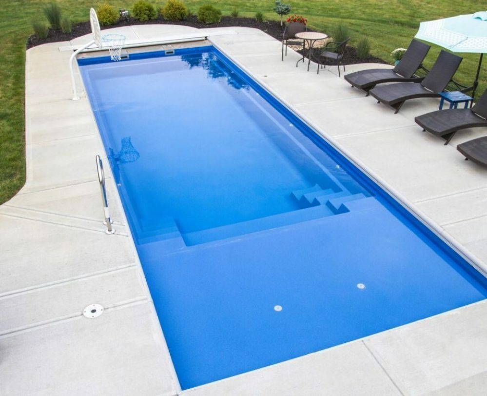 Rectangular backyard pool with blue water, white deck, and lounge chairs beside it