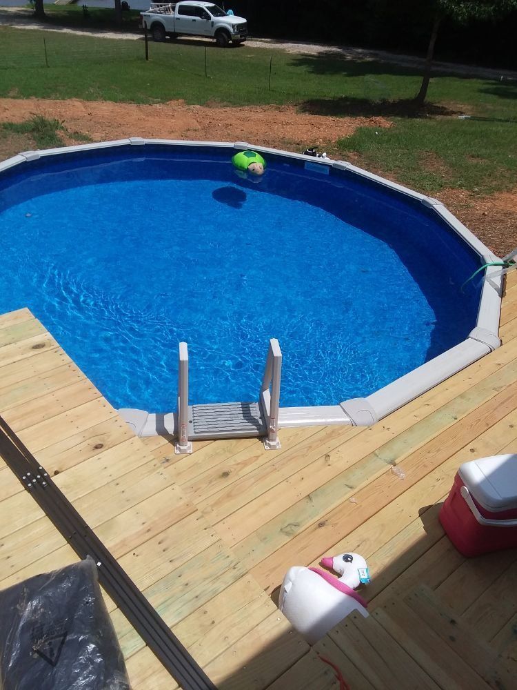 Backyard above-ground pool with blue water, wooden deck, and a small slide/ladder in the foreground