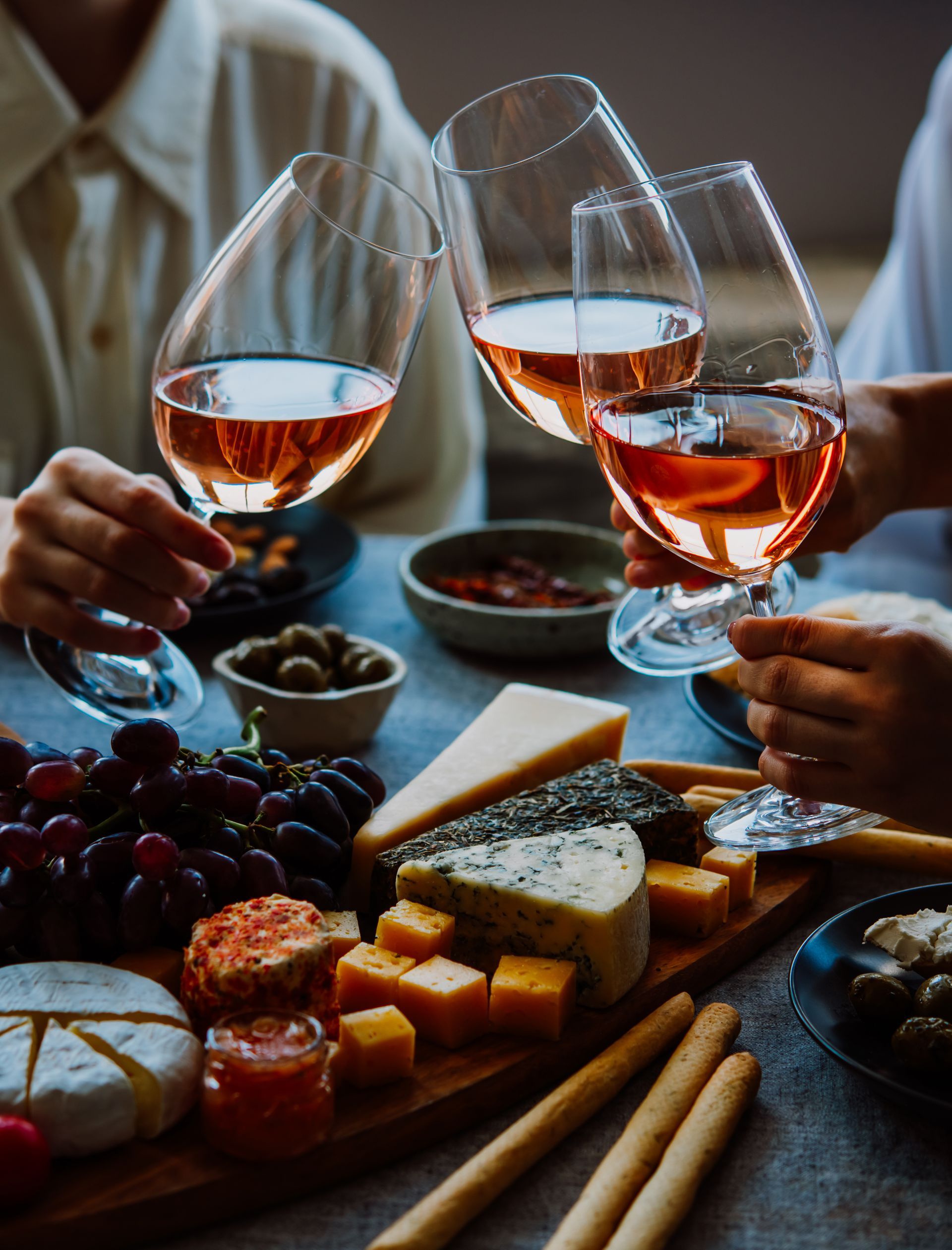 People toasting with glasses of rosé wine over a charcuterie board.