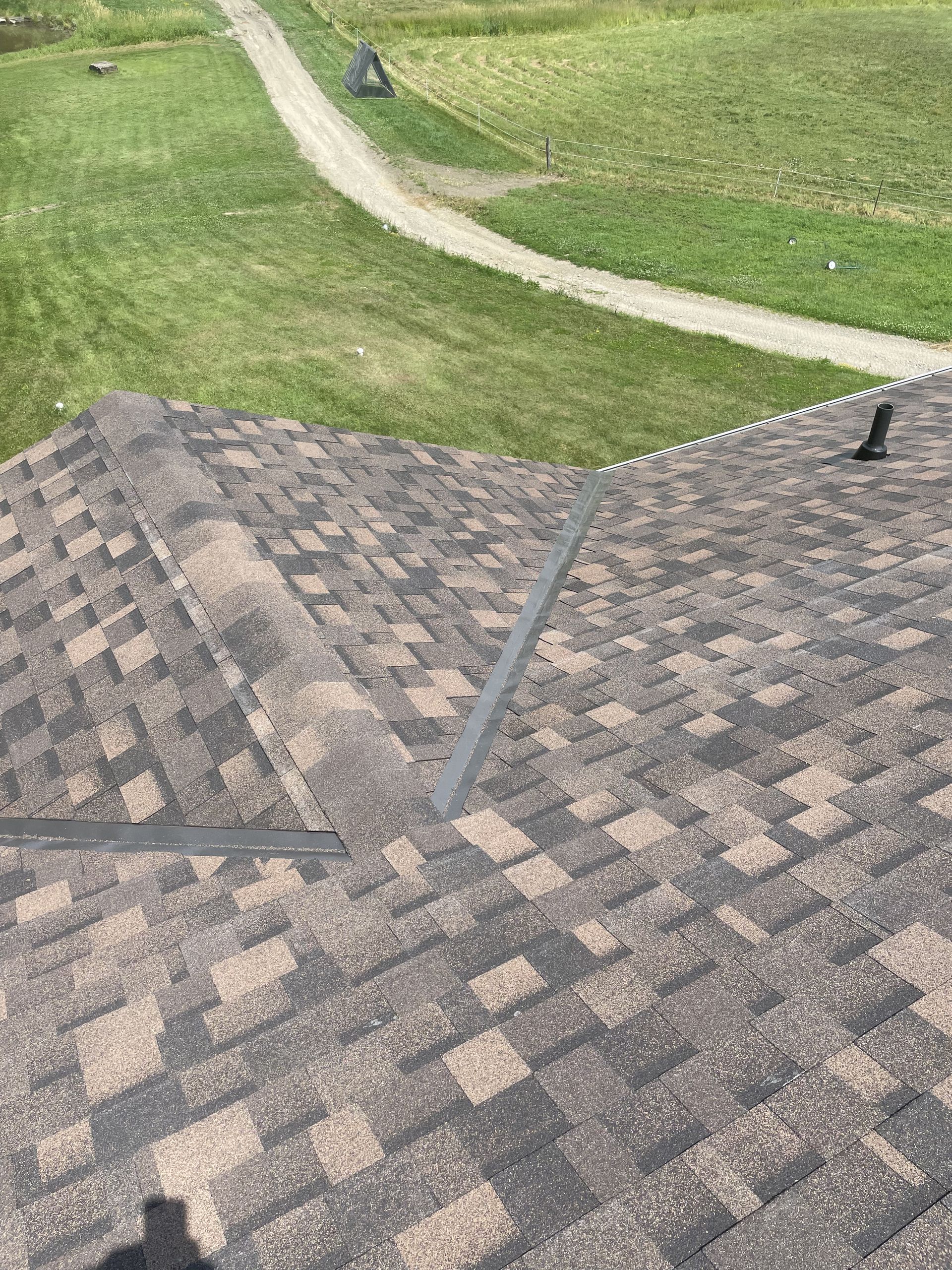 Roof with brown and black shingles, a metal flashing, and a dirt path in the background.