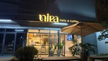 Fachada de noche de Nira Nails & Coffee con letrero iluminado