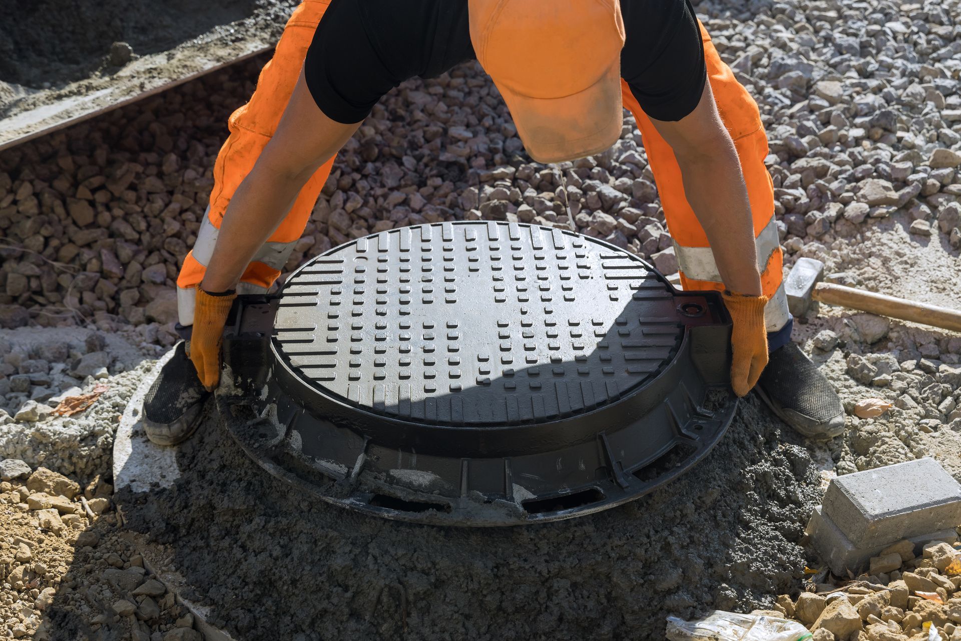 Worker in orange uniform placing a manhole cover on a concrete base.