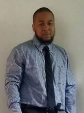 A man in a plaid shirt and tie is standing in front of a white wall.