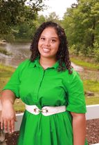 A woman in a green dress is standing next to a white fence.