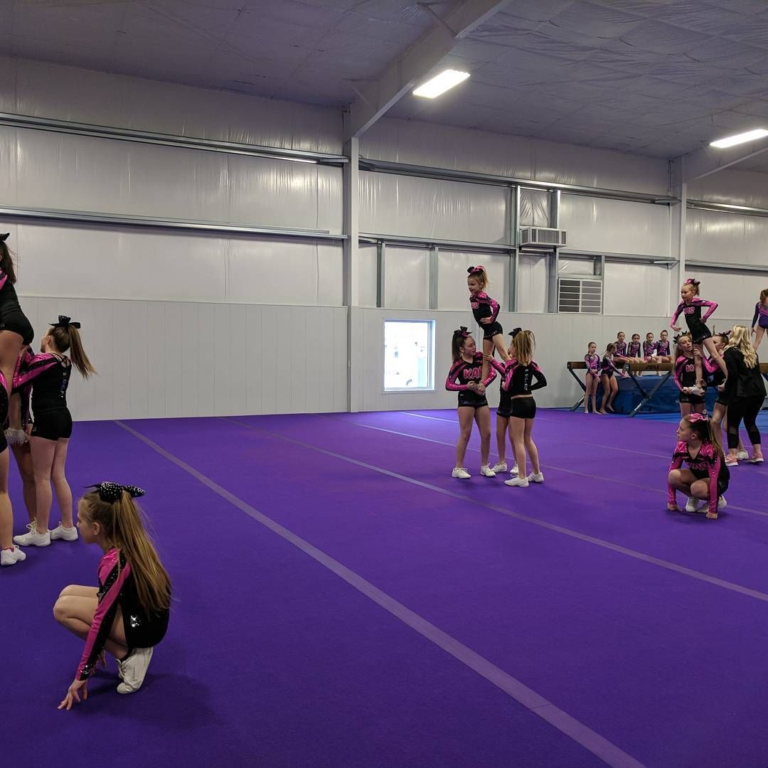 Cheerleaders performing stunts on a purple indoor mat in a gymnasium