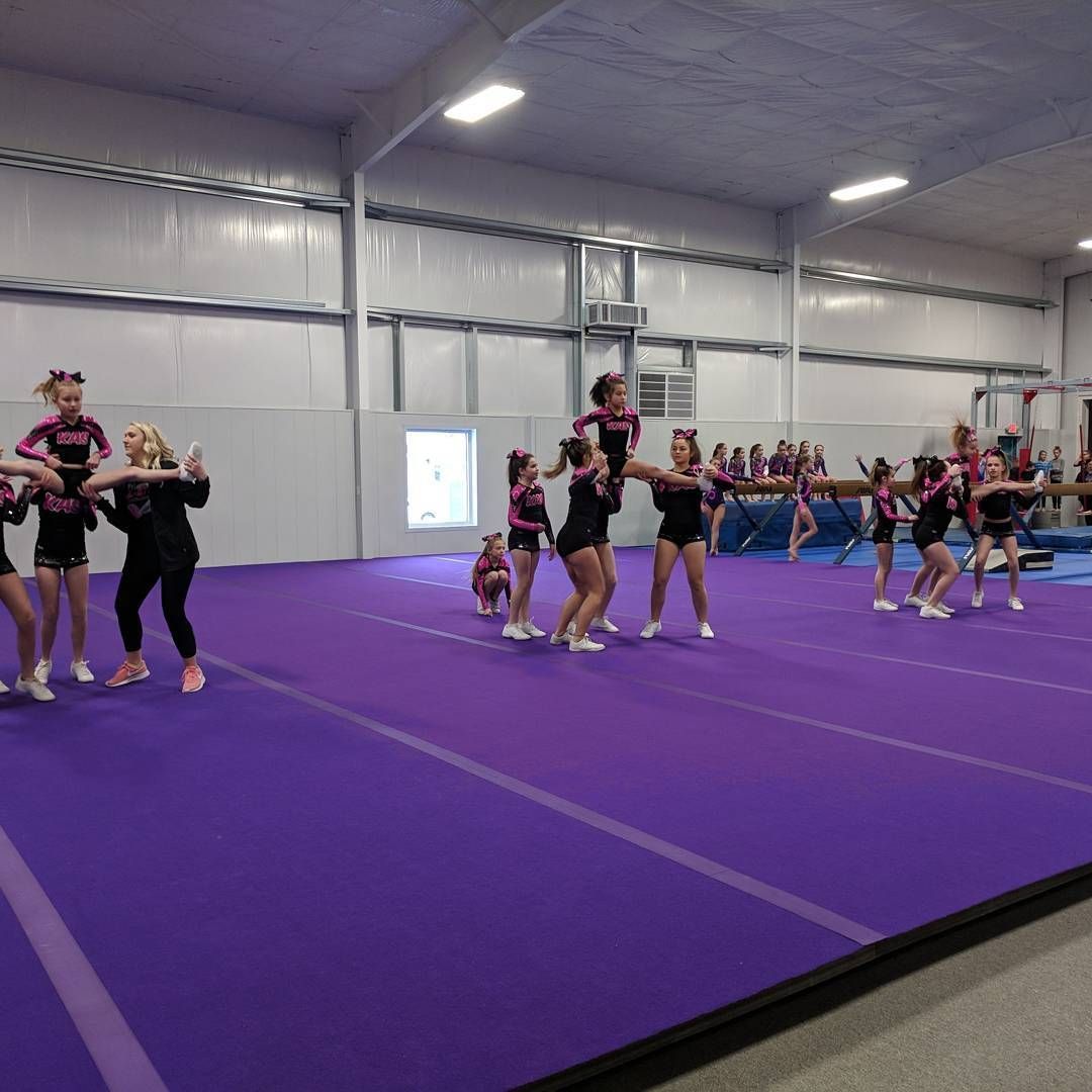 Cheerleading practice in a gym, with athletes performing on a purple mat