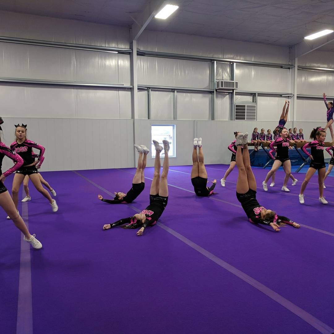 Cheerleaders practicing tumbling on a purple mat inside an indoor gymnasium