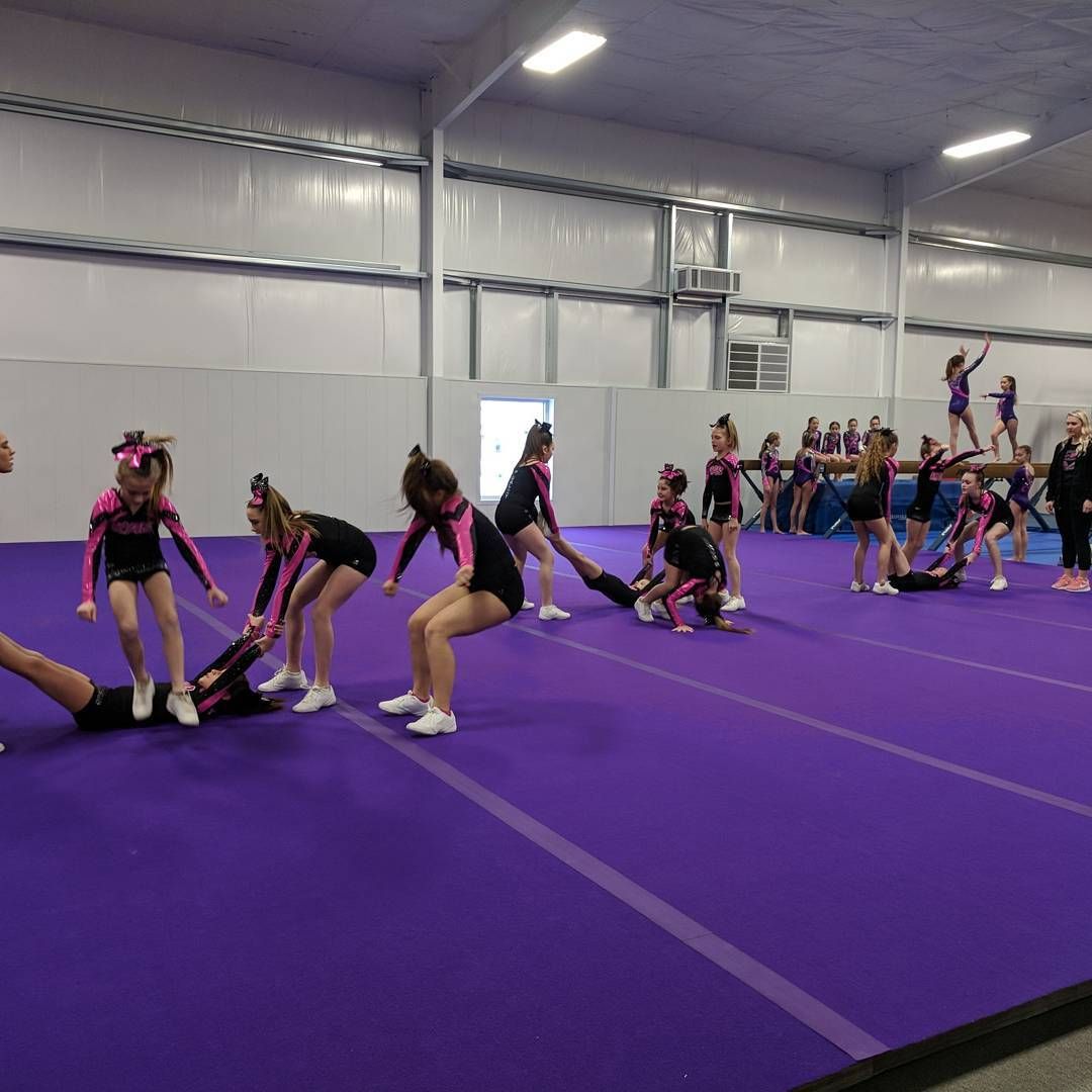 Cheerleaders practicing stunts on a purple mat inside an indoor gymnasium