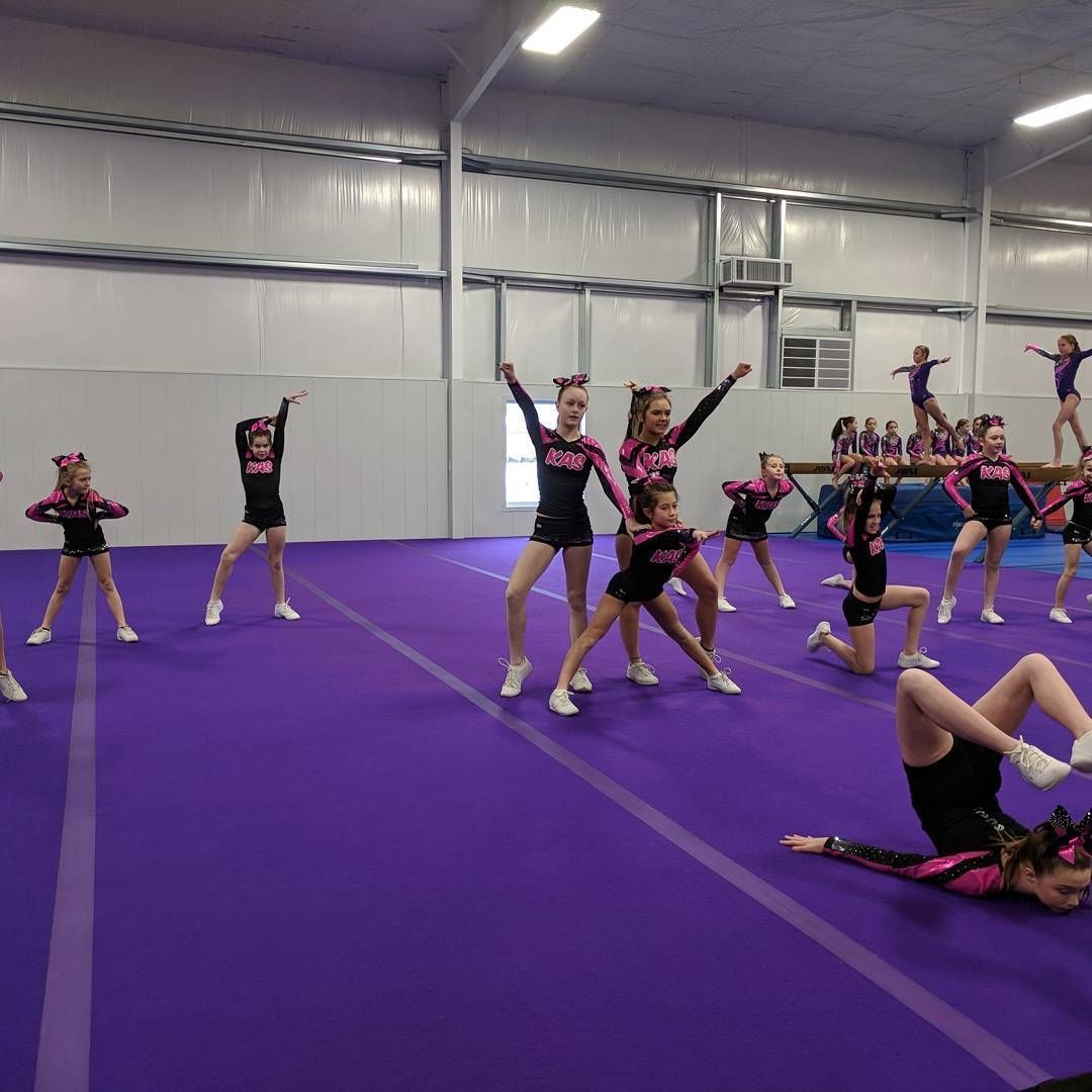 Cheerleaders practicing stunts on a purple gym mat in an indoor training facility