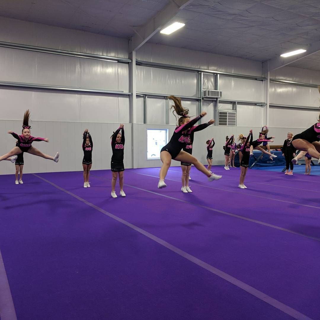 Cheerleaders practicing stunts on a purple mat inside a gymnasium