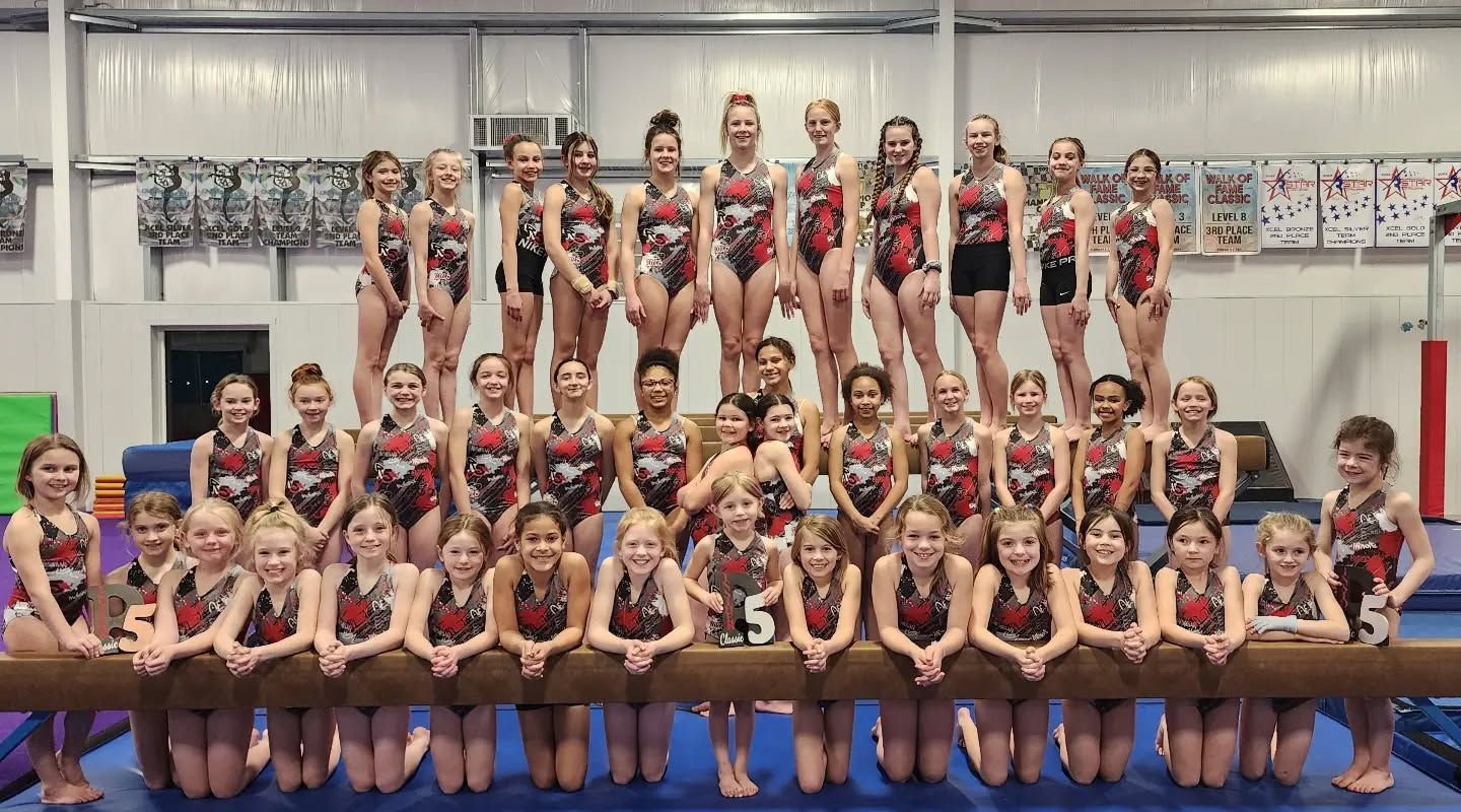 Large gymnastics team posing in matching red and black uniforms on mats in a gymnasium