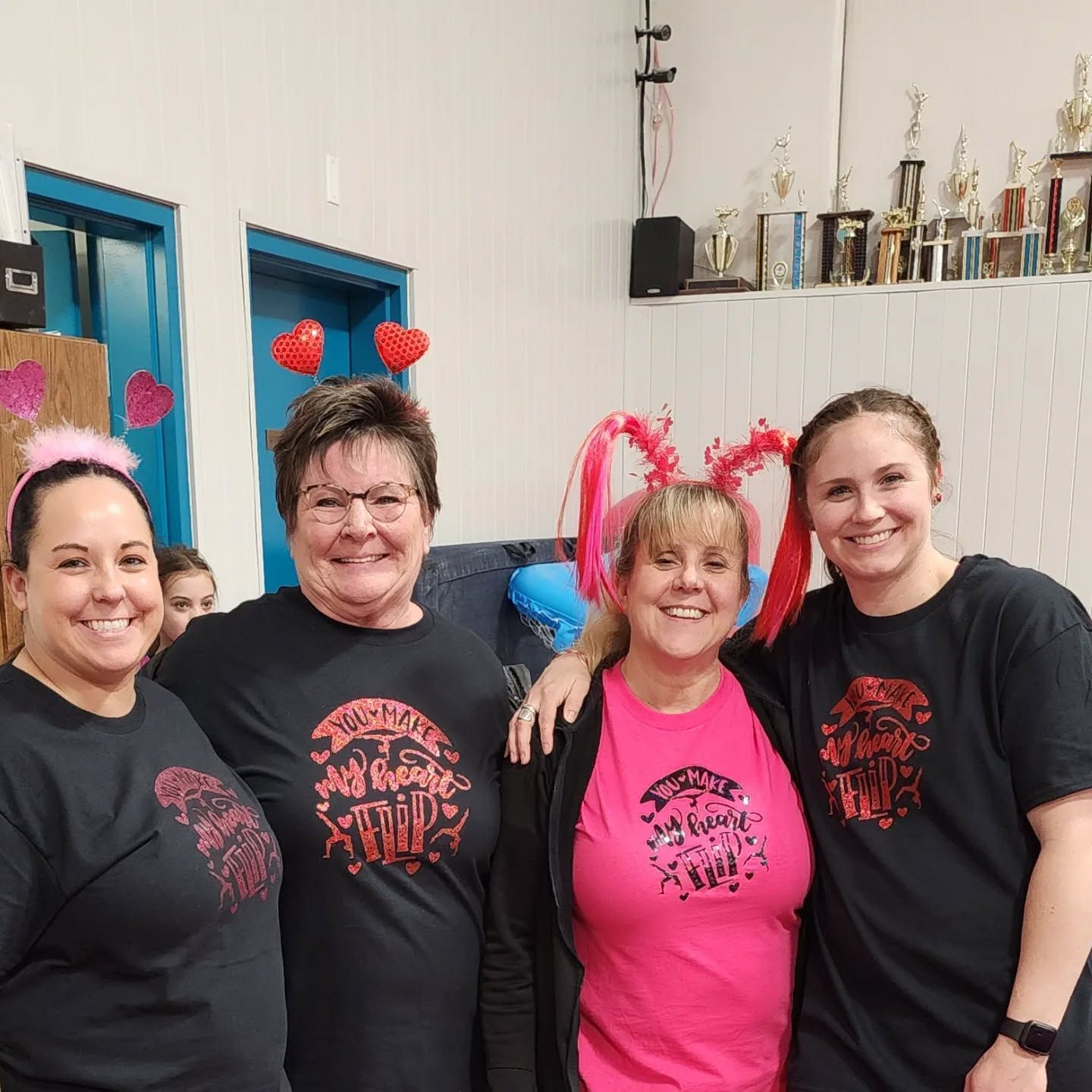Four people smiling indoors, wearing matching black and pink shirts at a festive gathering