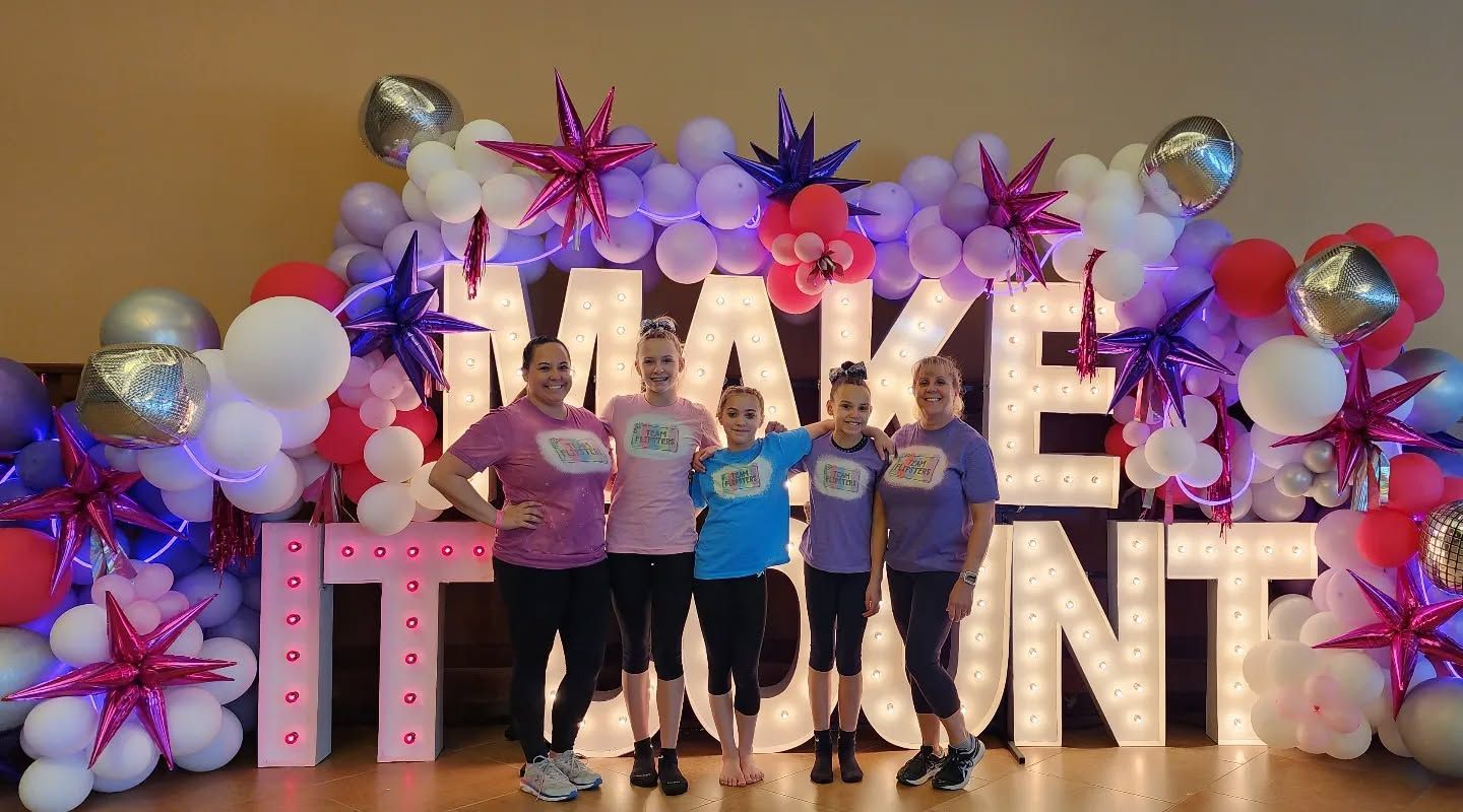 Group posing in front of a colorful “MAKE IT COUNT” balloon display with stars and balloons