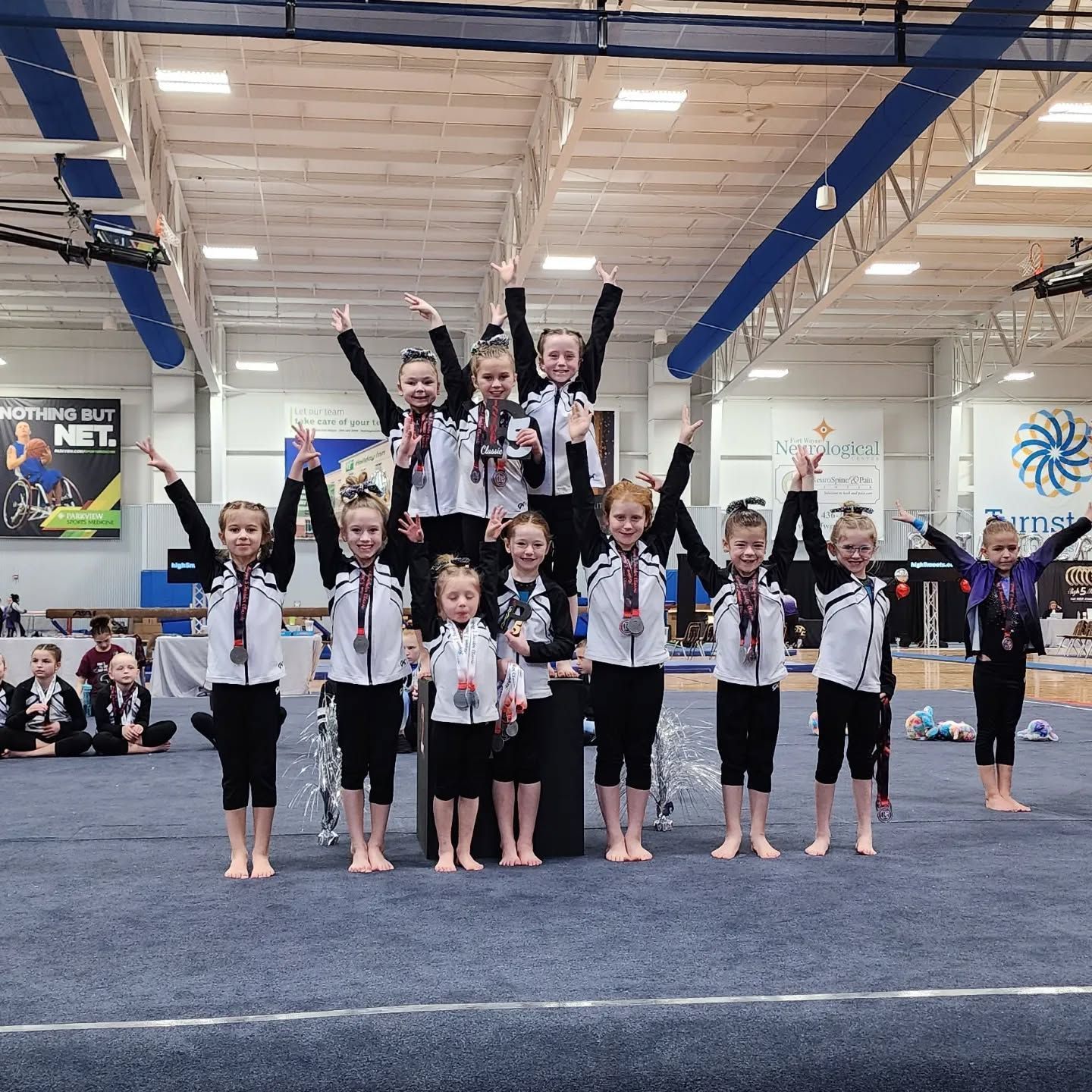 Gymnasts posing on mats in a gym, with several children standing on others’ shoulders and raising their arms