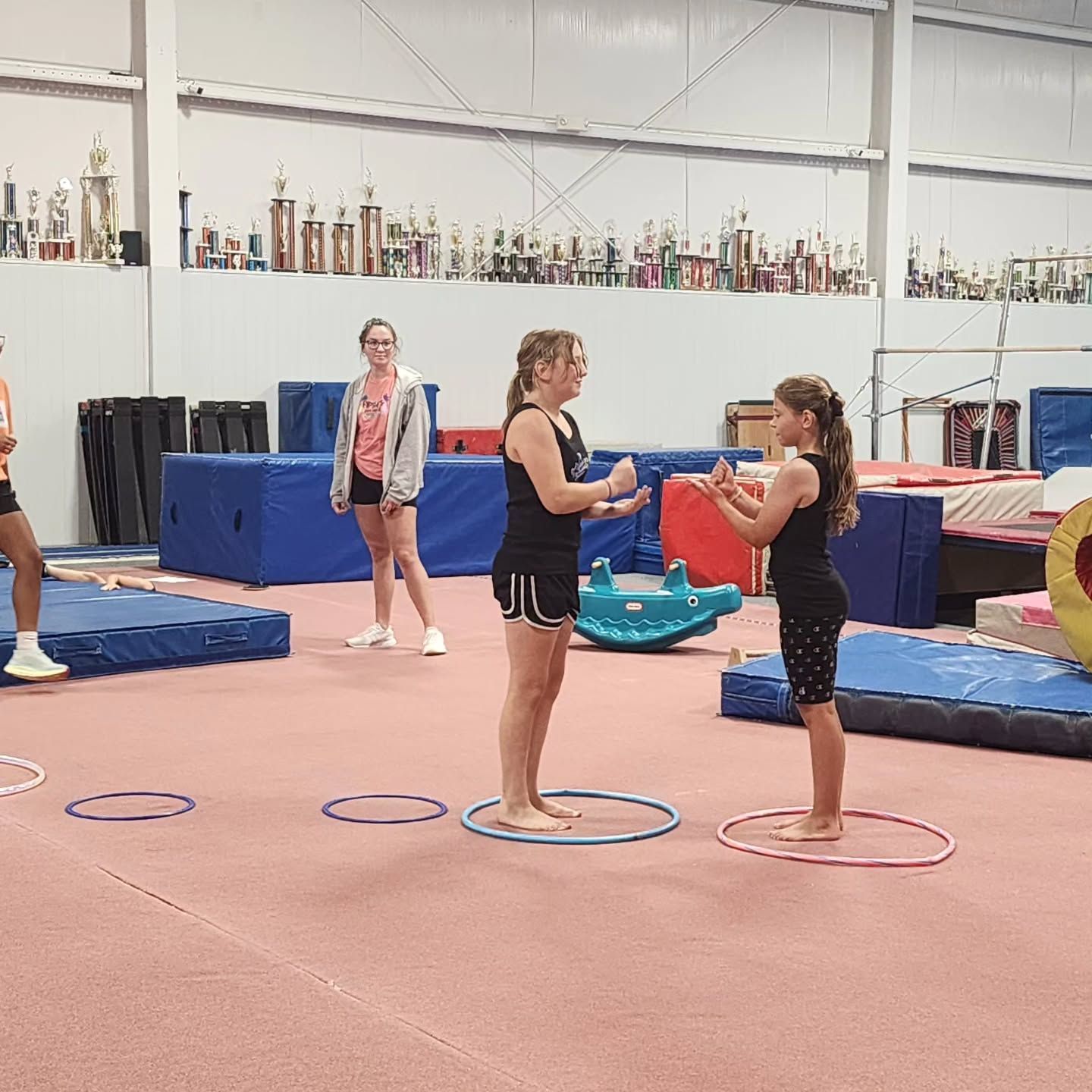 Two girls balancing on circles in a gym, facing each other during practice.