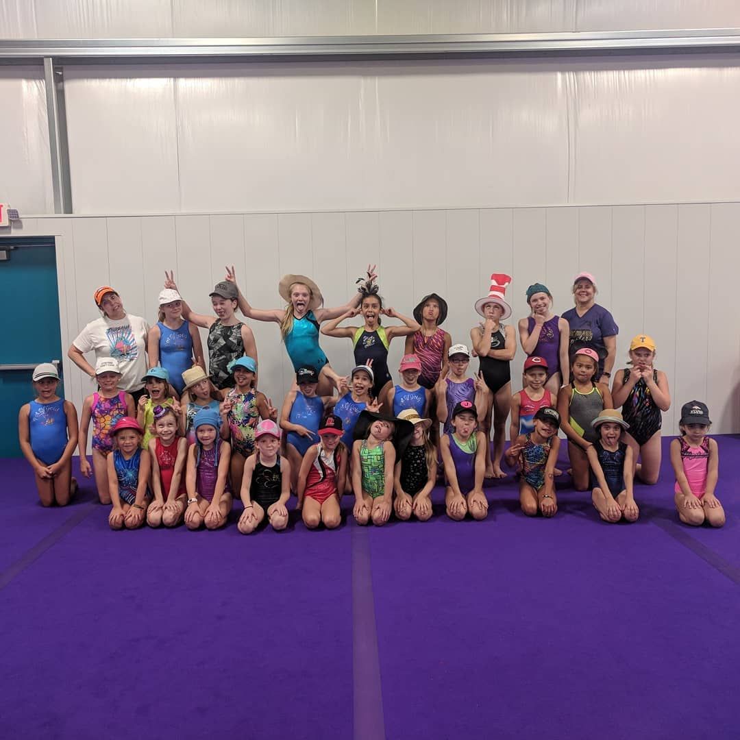 Group of children posing on a purple gym mat, many wearing colorful dance costumes and hats.