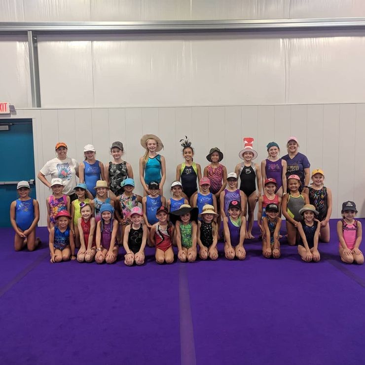 Large group of children posing in a gym on purple mats, some standing and some kneeling, wearing colorful outfits and hats
