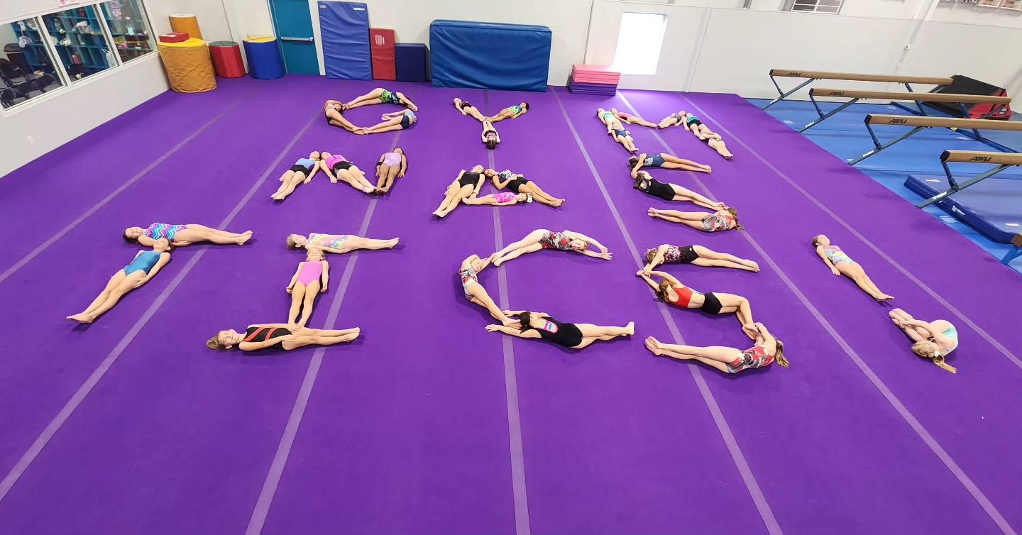 Gymnastics class forming letters on a purple mat in a gymnasium