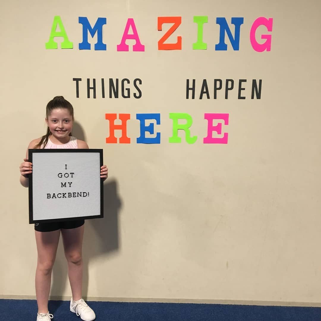 Girl holding a sign beside colorful wall text reading “AMAZING THINGS HAPPEN HERE.”