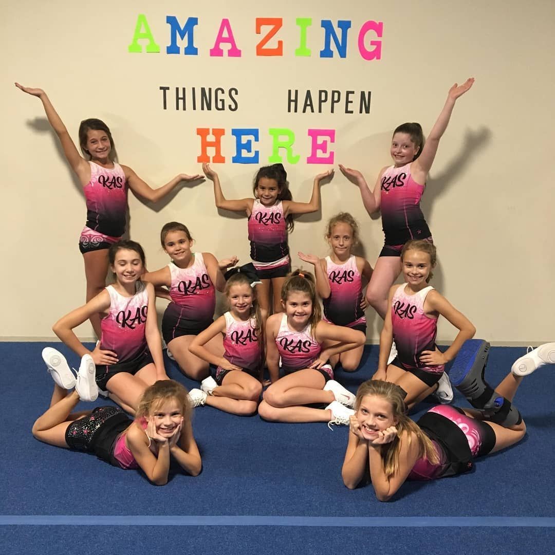 Cheer team posing on blue mat in front of “Amazing Things Happen Here” wall sign