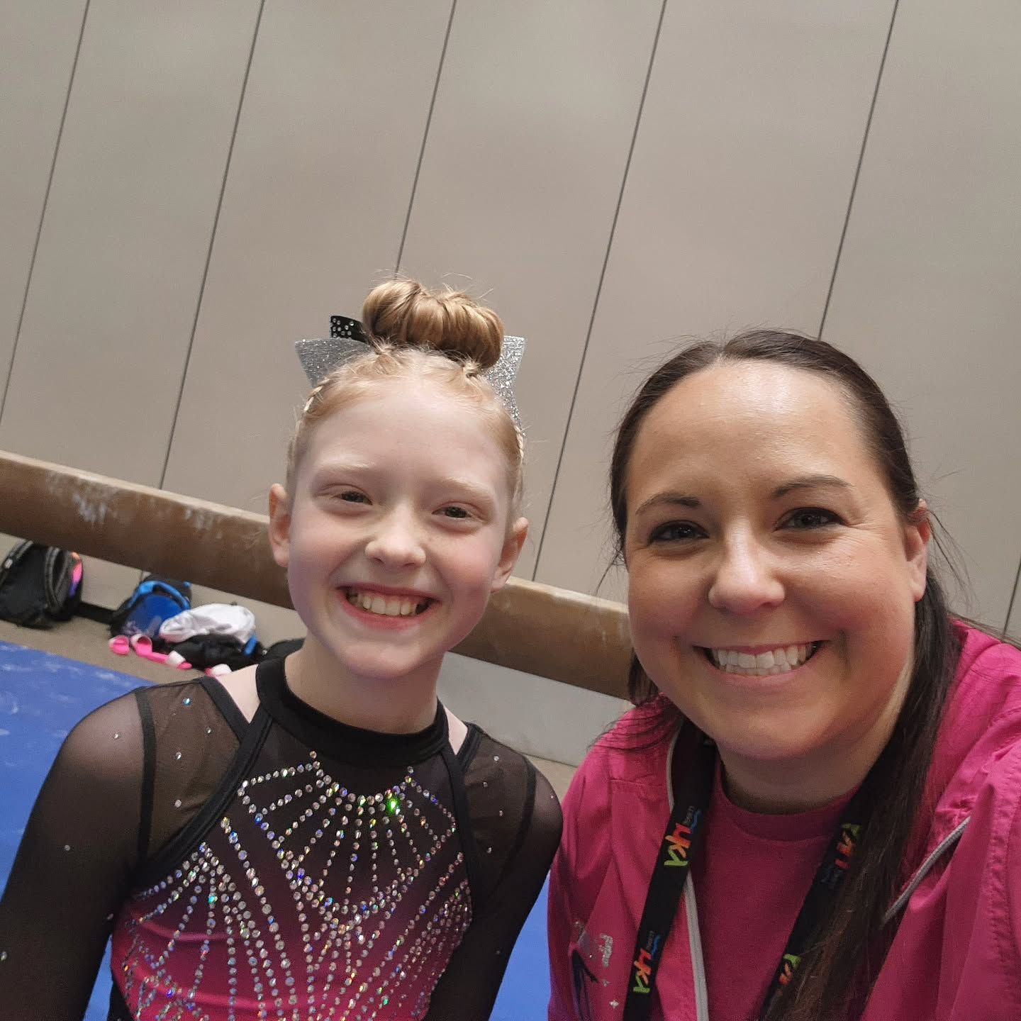 Two smiling people at an indoor event, one in a sparkly black costume and one in a pink jacket.