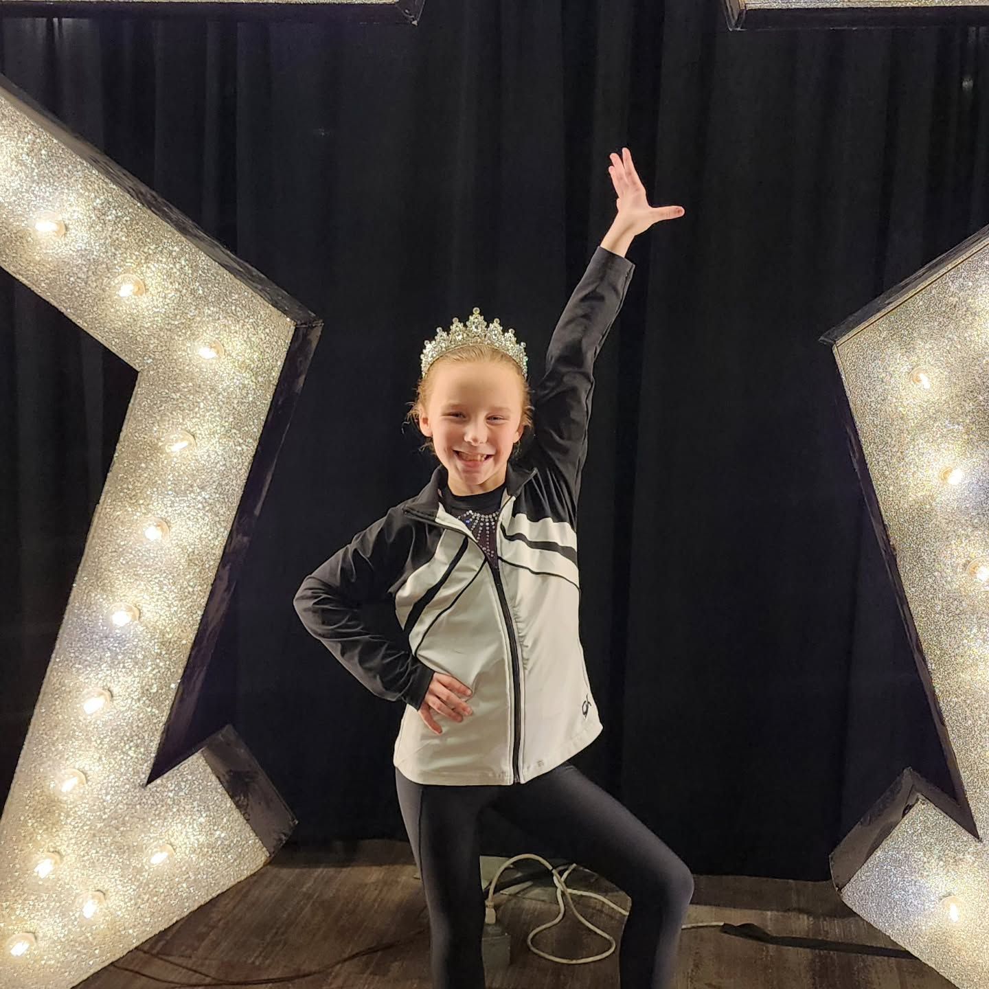 Smiling dancer posing with one arm raised between large illuminated letters on a dark stage
