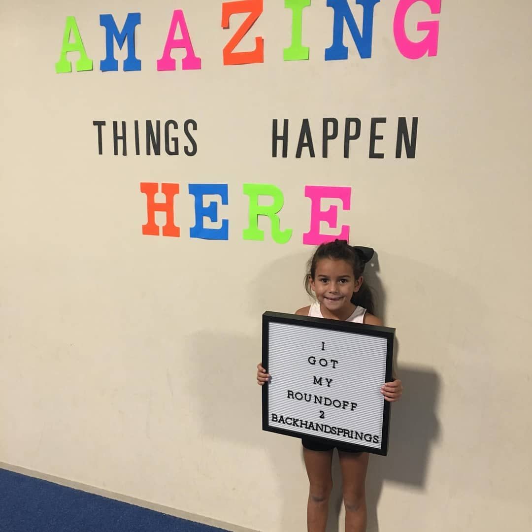 Girl holding a sign under colorful wall text reading “Amazing things happen here”