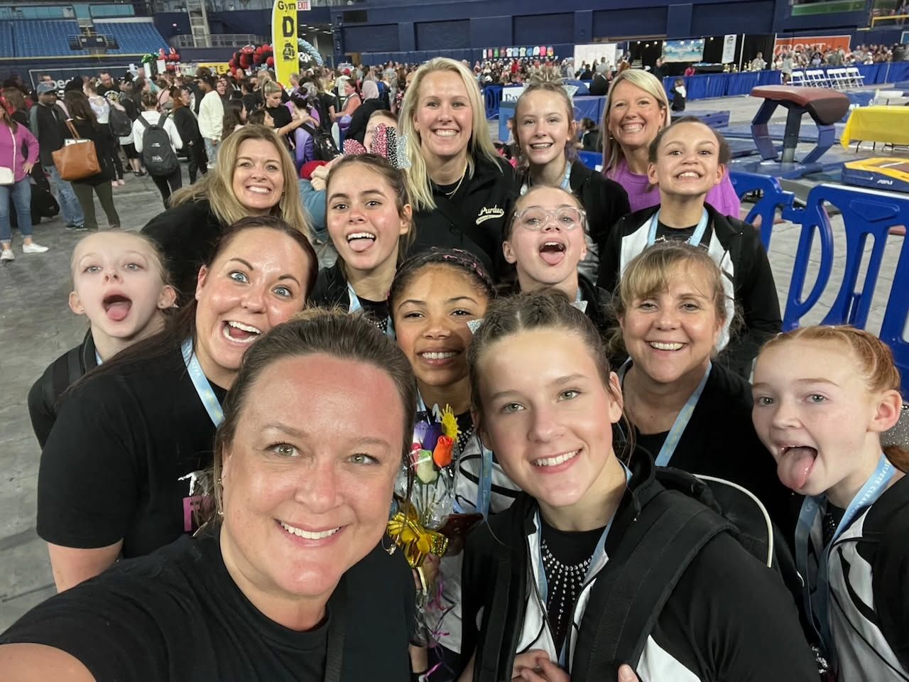 Group of smiling people posing indoors at a sports event, with blue barriers and a large hall in the background