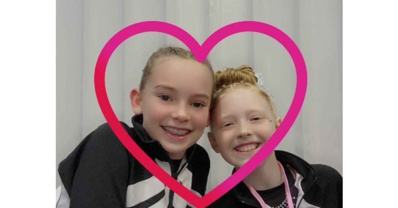 Two smiling children pose close together inside a pink heart outline.