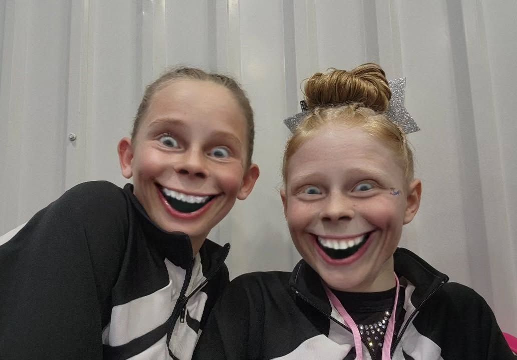 Two smiling people with exaggerated eyes posing in front of a white curtain