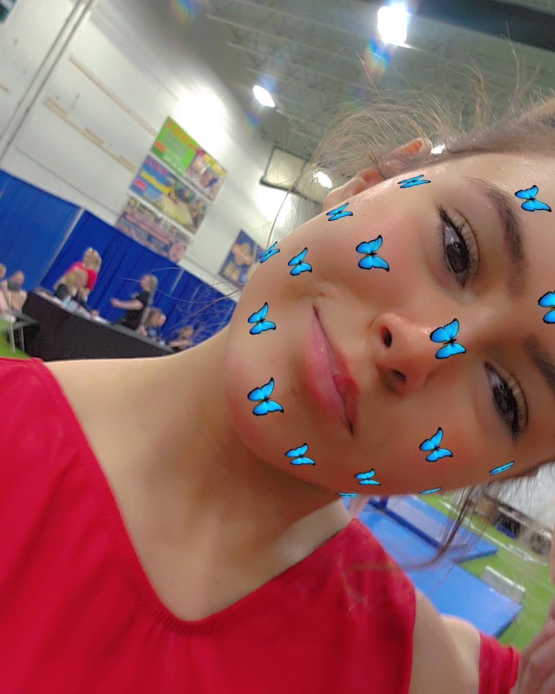 Smiling child in a red shirt indoors, with blue butterfly stickers on their face