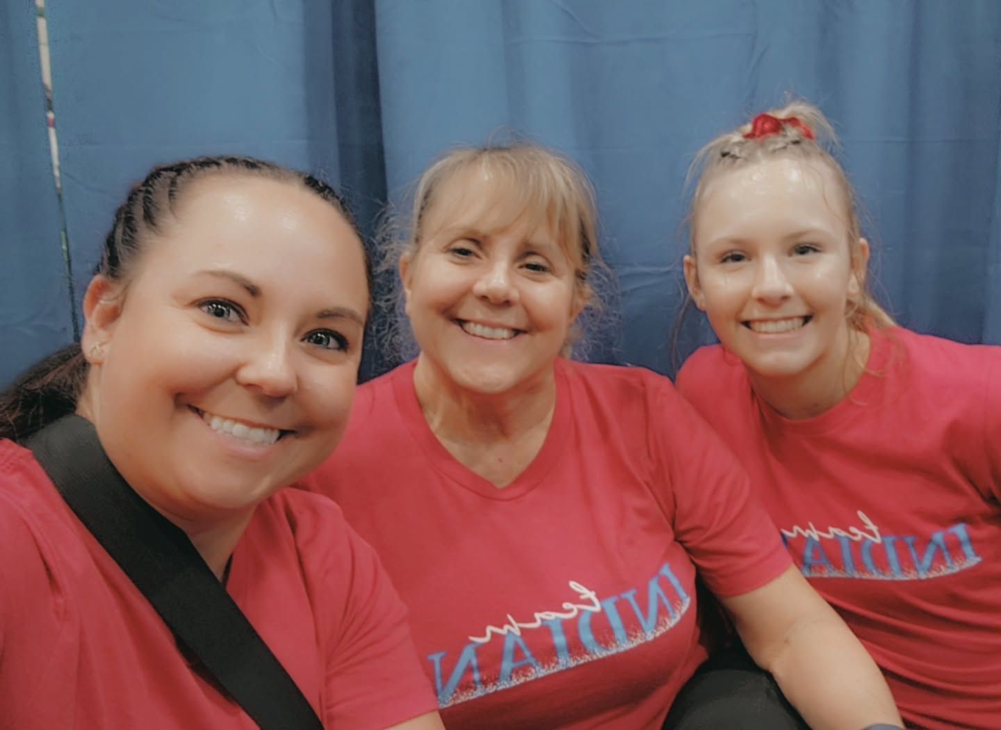 Three people smiling in red shirts, posing in front of a blue backdrop.