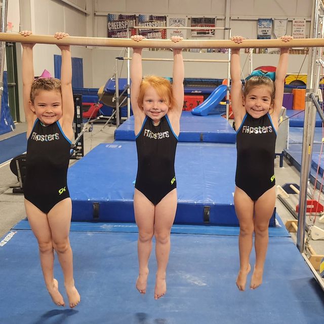 Three gymnasts hanging from a horizontal bar in a gymnastics gym, wearing black leotards.