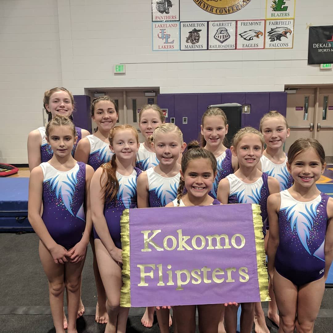 Team in purple leotards holding a “Kokomo Flipsters” sign in a gymnasium.