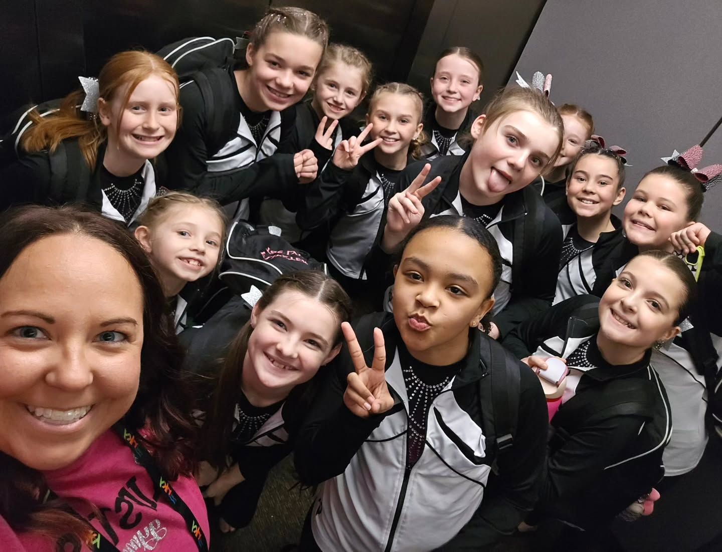 Cheering dance team group selfie in black and pink uniforms, smiling and making peace signs
