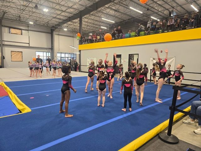 Cheerleaders performing in a gym on a blue mat, with arms raised during practice