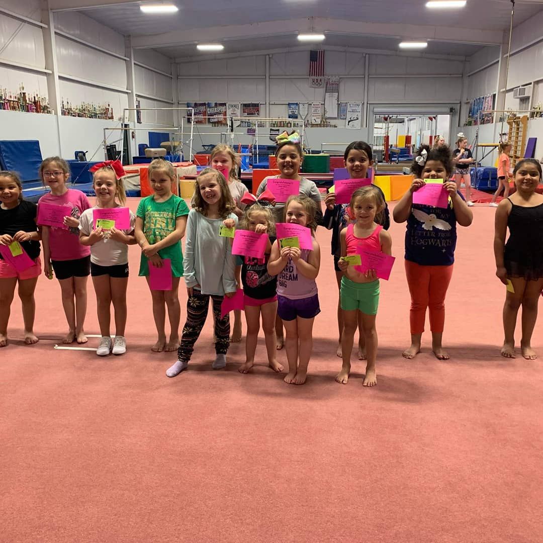Group of children in a gym holding pink certificates and posing on a red mat