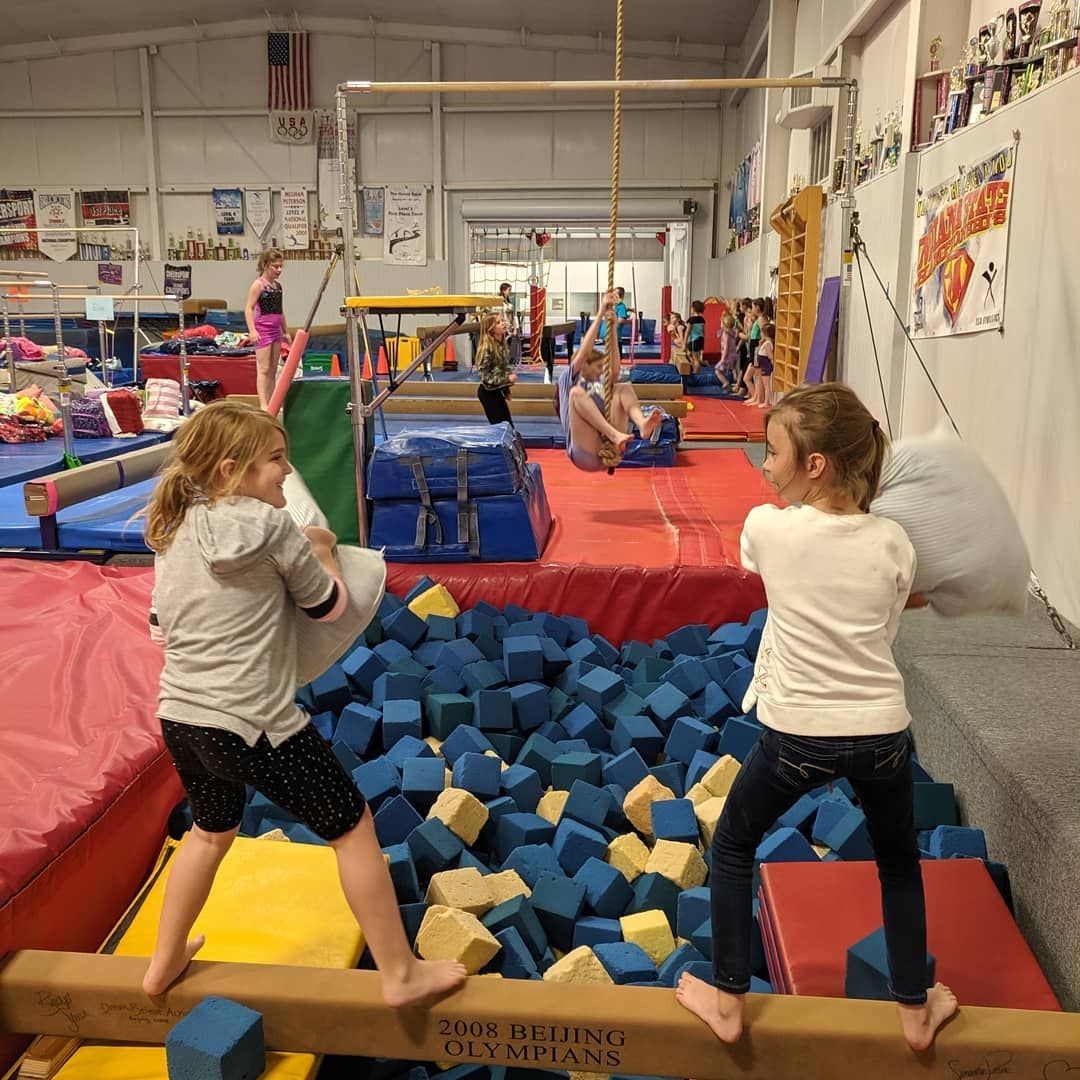 Children on balance beams over a foam pit in a gymnastics gym