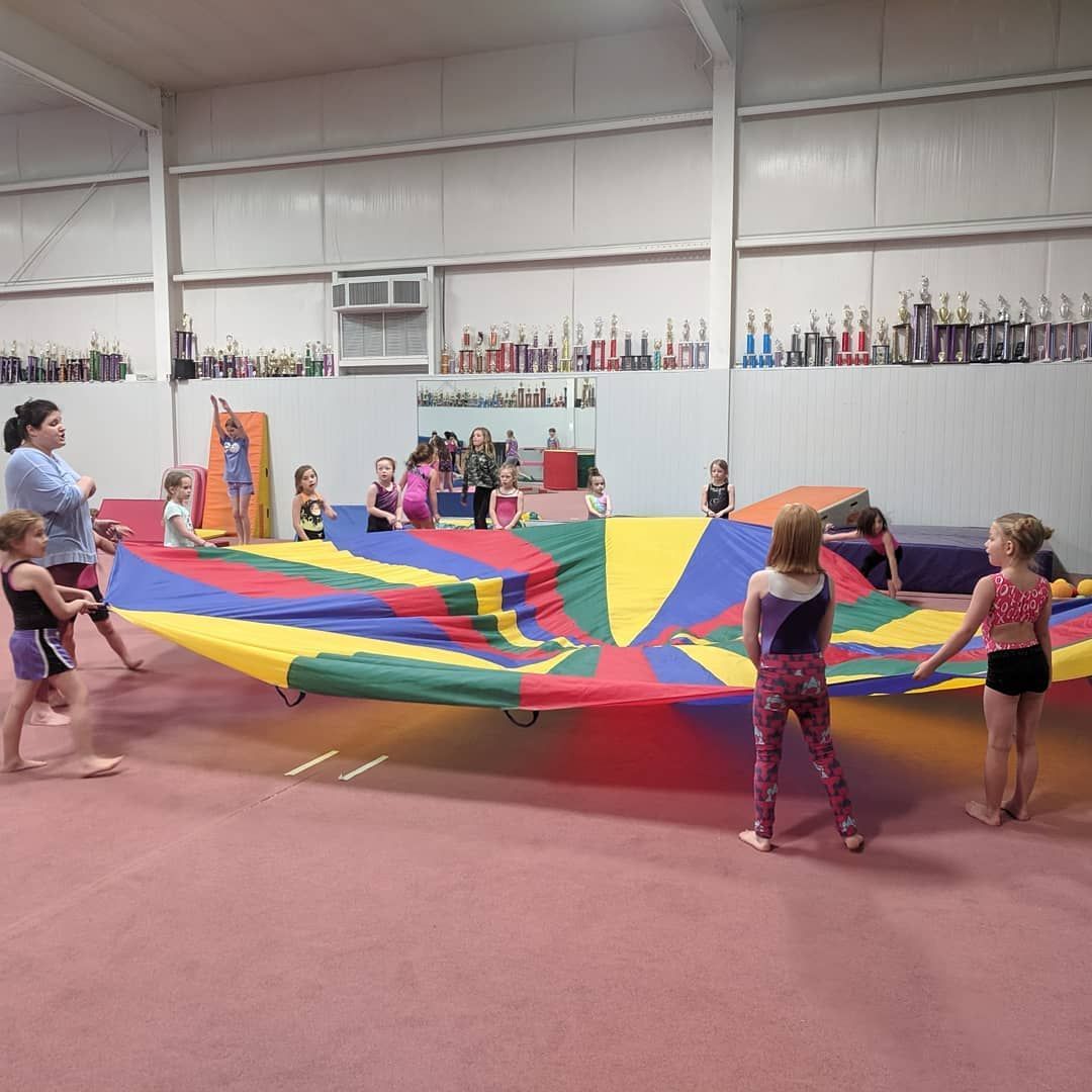 Children playing parachute in a gym with a colorful rainbow canopy.