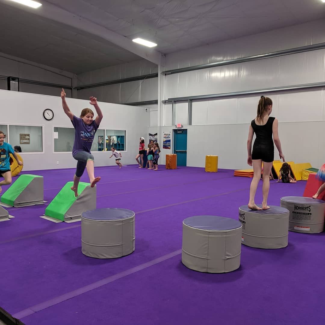 Children doing obstacle course activities in a purple-floored gym with padded blocks