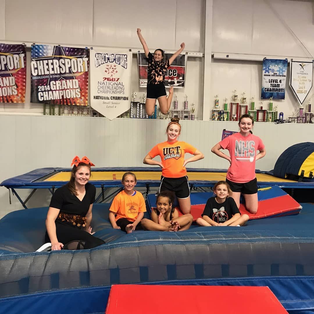 Cheer gym group posing on mats, with one athlete lifted high holding a trophy