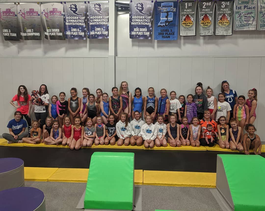 Large group posing on a gymnastics mat with colorful ramps and banners in the background.