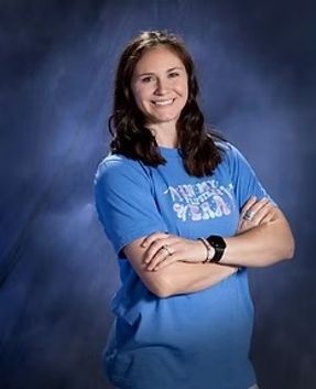 Smiling person in a blue T-shirt, standing with arms crossed against a blue studio backdrop